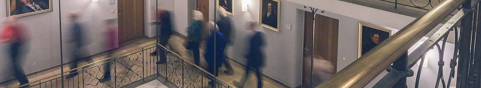 Verschwommene Aufnahme von Besucher*innen, die durch das Treppenhaus der Bayerischen Akademie der Wissenschaften laufen