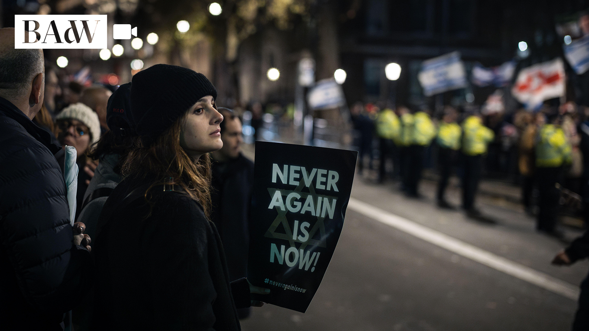 Junge Frau mit schwarzer Mütze und Schild "Never Again is now"